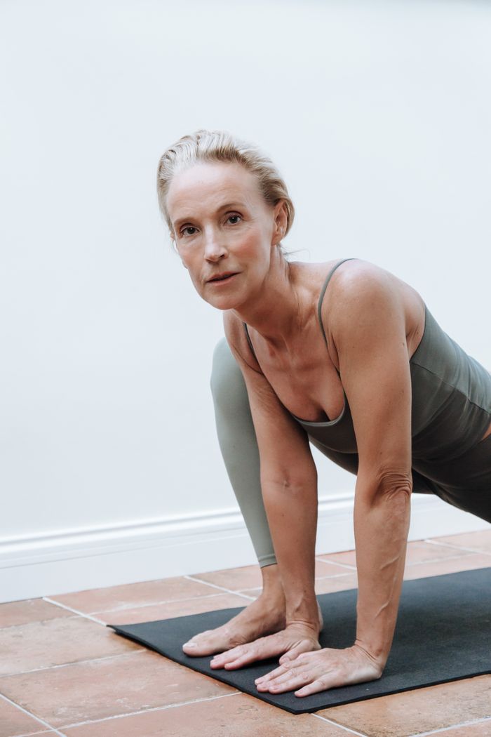 Senior woman in sportswear performing yoga on a mat indoors, demonstrating fitness and health.